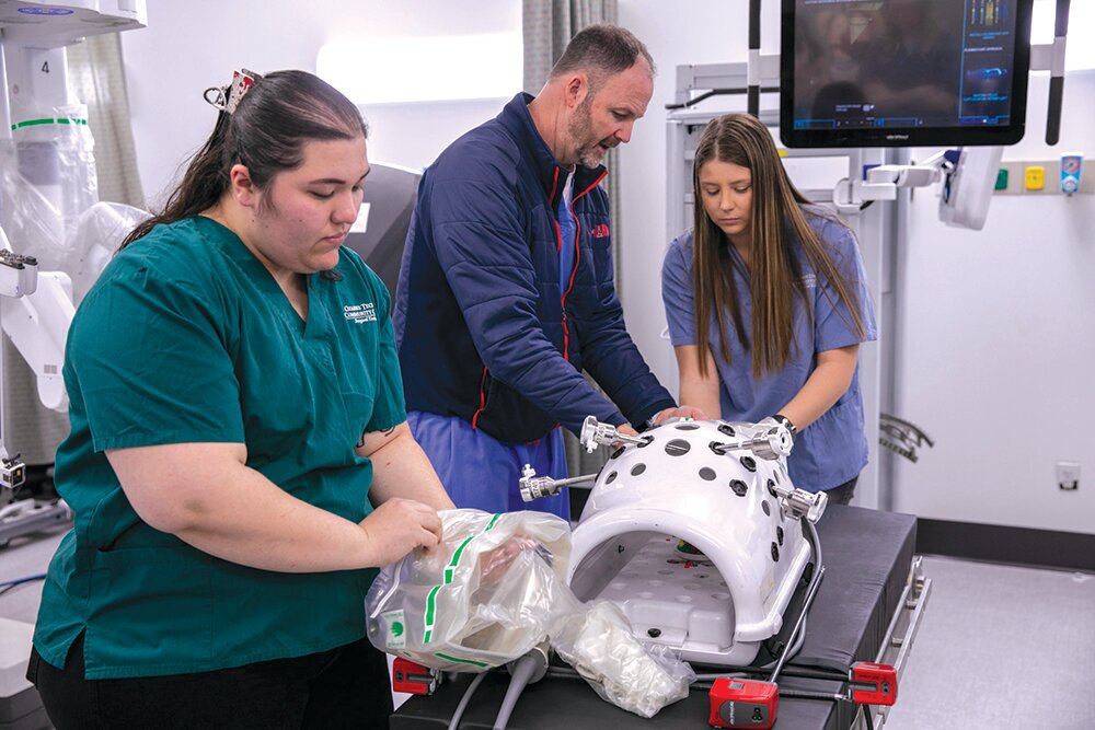 Erich Long with Intuitive Surgical Inc. discusses the company's da Vinci surgical robot with OTC students Malissa Bray, left, and Kaleigh Gautieri.